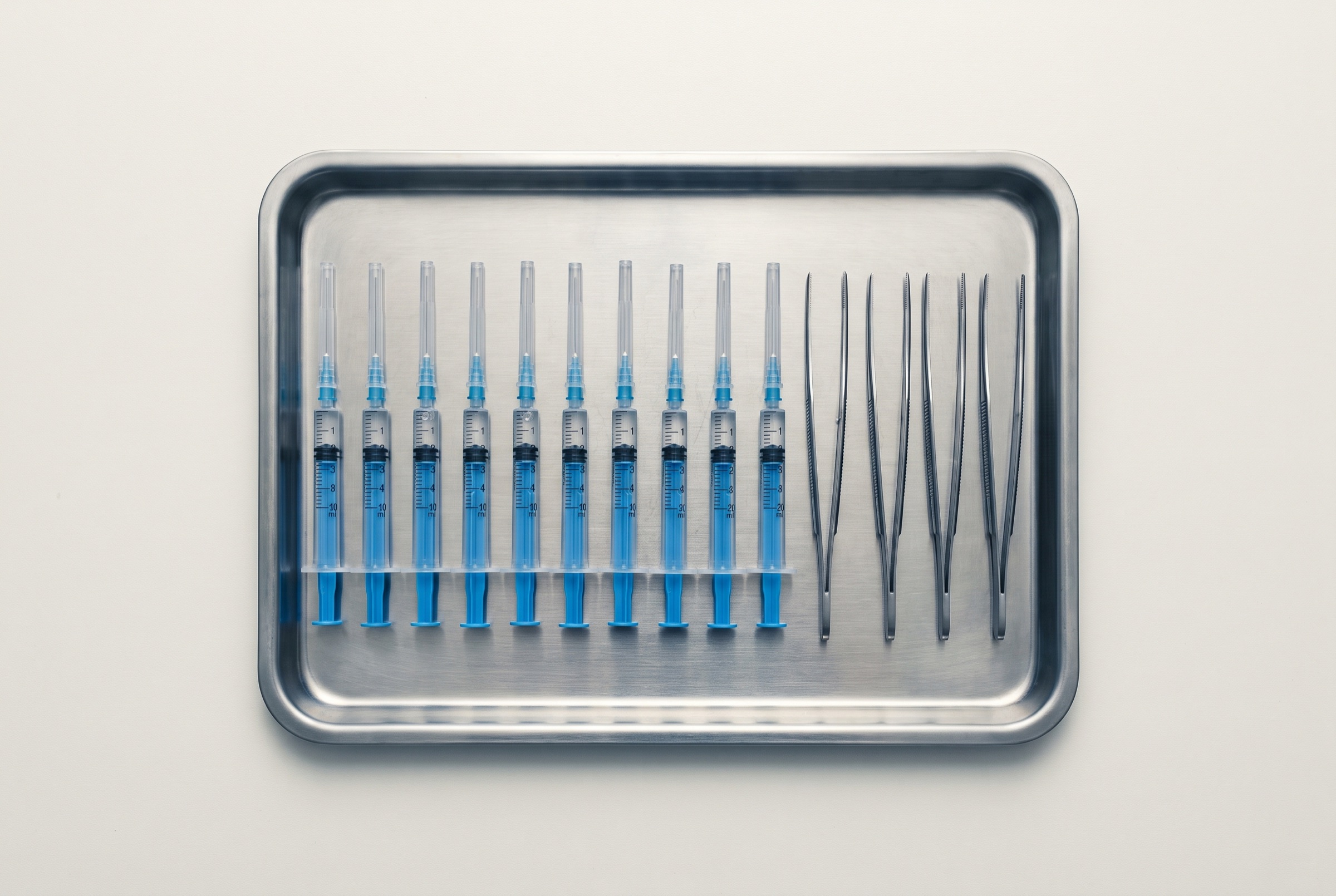 Instruments laid out in a precise row on a steel tray under cool, hard light
